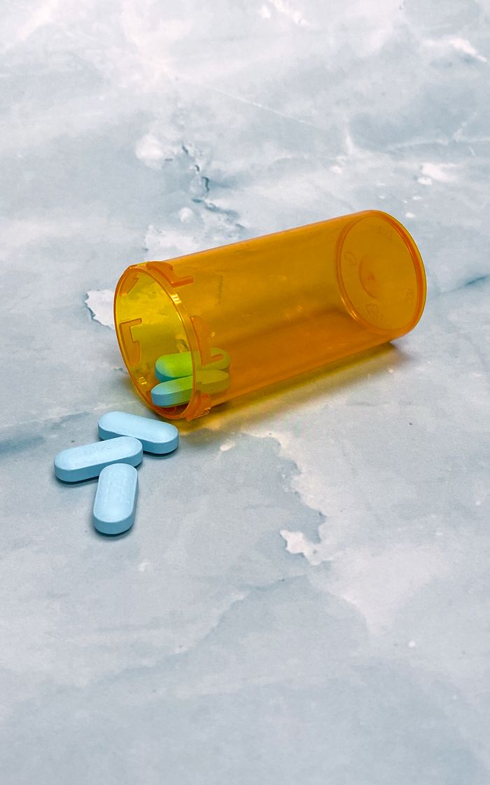 An orange pill bottle spilled, displaying blue tablets on a smooth marble surface, emphasizing healthcare and medication themes.