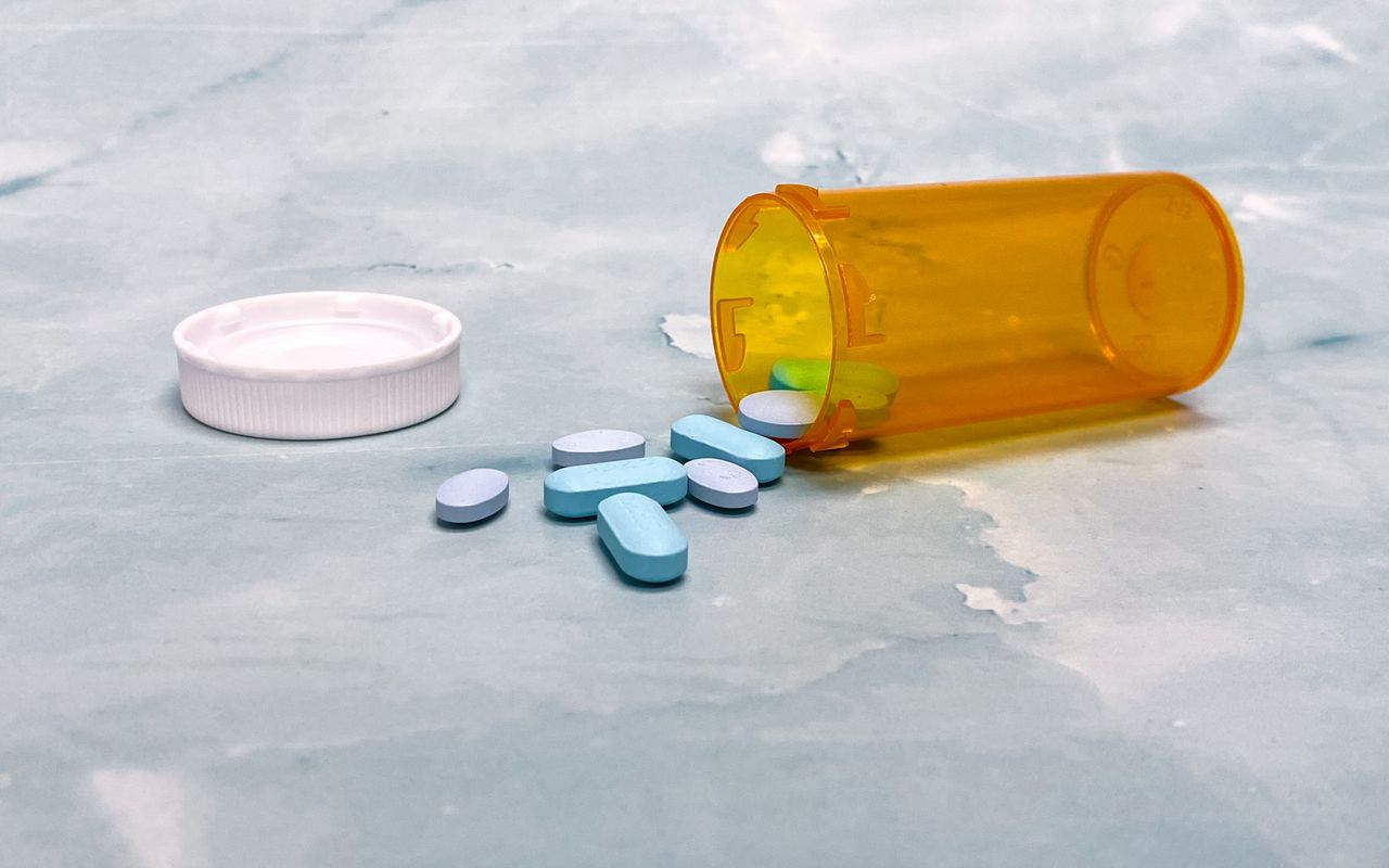 Home Scattered blue pills and an orange prescription bottle on a light surface.