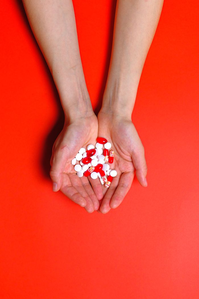 Home Close-up of hands holding multiple red and white pills on a vibrant red background.