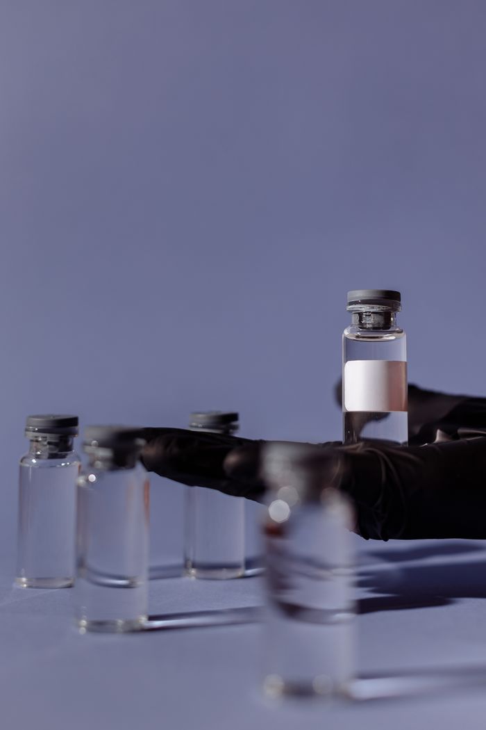 Close-up of vaccination vials with medical gloves holding one, against a soft blue background.
