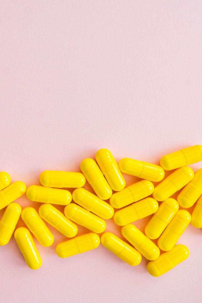 Bright yellow capsules scattered on a soft pink surface, perfect for health-related content.
